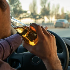 Driver holding alcohol behind the wheel, depicting legal risks of a first-time OUI offense in Massachusetts.